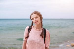 un hipster niña con trenzado pelo en coletas es caminando a lo largo el playa en ropa. verano concepto, ocio turismo foto