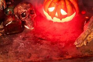 Halloween. Scary Halloween pumpkin with carved face on table in dark room with human skull and animal skull photo