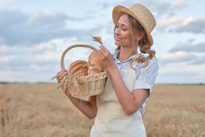 Female farmer standing wheat agricultural field Woman baker holding wicker basket bread product photo