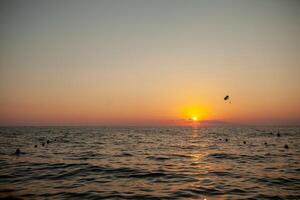 Silhouette of powered paraglider soaring flight over the sea against marvellous orange sunset sky. Paragliding - recreational and competitive adventure sport. photo