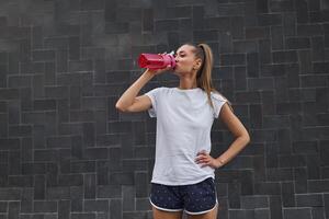 Woman drink water red bottle after morning workout city background photo