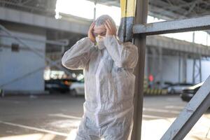 Despair healthcare worker in white covid protective overalls. Tired Male caucasian doctor grabs his head cower in depression during coronavirus pandemic photo