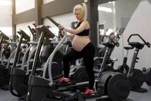 embarazada mujer formación el embarazo elíptico entrenador en gimnasio cardio ejercicios en corriendo simulador foto