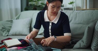 Footage slow motion shot, Asian teenager woman sitting on sofa packing travel luggage with personal items for traveling trip, Preparation travel suitcase at home. video