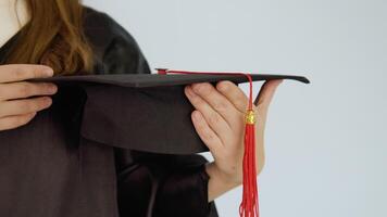 A square black hat with a red brush in the hands of a caucasian graduate with neat natural nails. Close-up shooting of a hat and hands. White background video