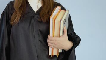 Several textbooks in vertical position in the hand of a female student in a black robe. View of books and hands up close on white background. video