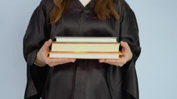 Several textbooks in horizontal position in the hands of a caucasian female student in a black robe. View of books and hands up close on white background. video