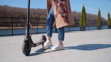 une Jeune fille étudiant dans jeans et une manteau approches le électrique scooter et départs équitation sur il. moderne gadgets pour Jeune gens et affaires personnes. écologique ville transport video