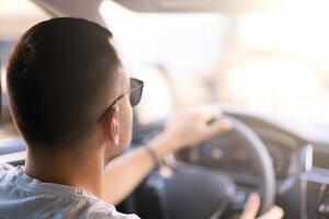 Young Caucasian man sitting in a car rear view holding the steering wheel watching the translation on a bright sunny day photo