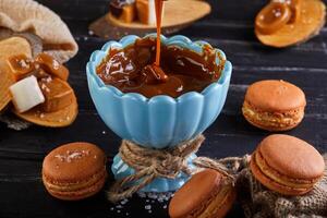 Caramel being drizzled over macarons in a wooden bowl photo