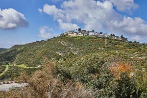 Rocky hill with a dirt road in front under a blue sky with white clouds and a modern villa on top photo