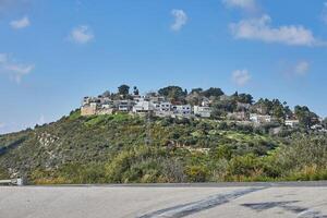 Rocky hill with a dirt road in front under a blue sky with white clouds and a modern villa on top photo