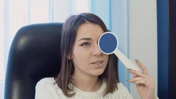 un joven caucásico mujer en un acogedor blanco suéter en el del oftalmólogo oficina a el óptica clínica respuestas un del doctor pregunta durante un visión prueba. video