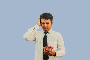 Adult Asian man doing thinking gesture while holding Indonesia paper money photo