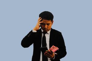 Adult Asian man doing thinking gesture while holding Indonesia paper money photo
