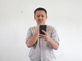 Asian man holding his mobile phone with serious expression photo