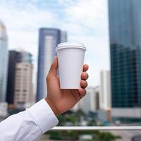 AI generated Hand holding white paper cup mockup with cityscape background photo