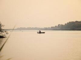 Boat on the calm lake with fisherman and reed at sunrise photo