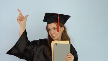 A young female student in a black robe and a master's hat shakes books, which she holds in her hands. White background video