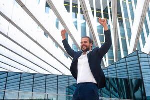 Excited young businessman in suit celebrating victory arms raised photo