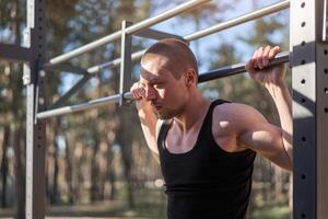 hermoso caucásico hombres levantar al aire libre rutina de ejercicio cruzar formación Mañana bombeo arriba brazo hacer ejercicio Deportes suelo naturaleza bosque foto