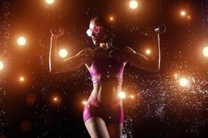 Beautiful sportswoman posing with dumbbells on a black background in spray of water photo