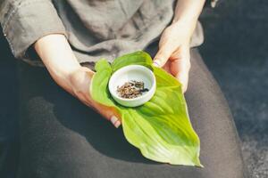 Dry tea leaves in a white saucer. Unrecognizable woman holding a bowl of tea in his hands showing it to the camera photo