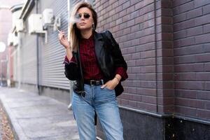 Beautiful young stylishly dressed Caucasian girl smokes cigarette on the street. photo