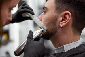 Young beautiful caucasian woman hairdresser cuts beard  handsome man at modern barbershop photo