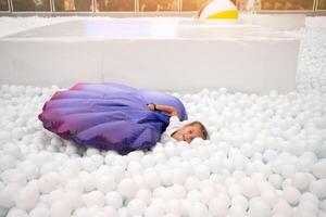 contento pequeño niña jugando blanco el plastico pelotas piscina en diversión parque. patio de recreo para niños. foto