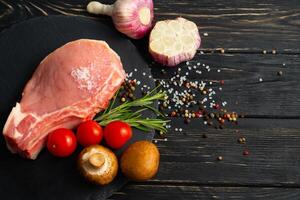 Top view of one pieces raw pork chop steaks with cherry tomatoes Champignon mushrooms on a black stone cutting board. photo