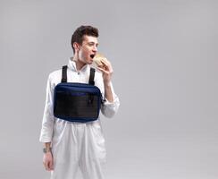 joven elegante masculino trabajador con cofre plataforma bolso es comiendo un sabroso jugoso hamburguesa en un blanco antecedentes foto