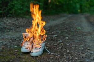 Used white high sneakers burning on a rural road that runs in the forest. photo