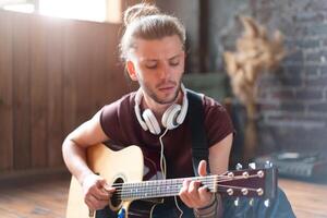 Handsome young man playing acoustic guitar sitting floor living loft room photo