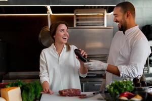 Handsome young African chef is cooking together with his Caucasian girlfriend in the kitchen using red wine as an ingredient. photo