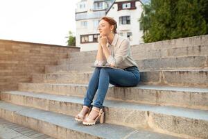 A beautiful young redhaired girl writes a romantic love letter sitting on a stairs near the institute. Student love. Or homework photo