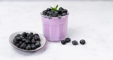 Tasty fresh blueberry yoghurt shake dessert in glass standing on white table background. photo