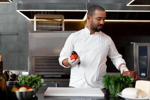 contento sonriente cocinero prepara carne plato con varios vegetales en el cocina. en uno mano el hombre sostiene verduras, en el otro un pedazo de Fresco carne foto