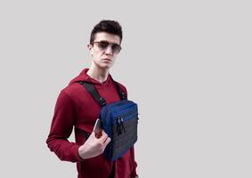 Young handsome guy in sunglasses and red hoodie with a chest rig bag posing in the studio on a white background photo