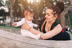 A beautiful smiling young brunette woman with long dreadlock hair hold a pretty baby. Mother looks tenderly at the child. They are in the green summer forest. photo