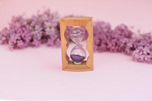 Sand running through the bulbs of an hourglass measuring the passing time in a countdown to a deadline, on a flower lilac spring background with copy space. photo