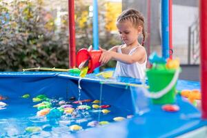 Child Fisher Catching Plastic Toy Fish On Pool Amusement Park Summer Day photo
