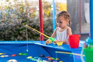 Child Fisher Catching Plastic Toy Fish On Pool Amusement Park Summer Day photo