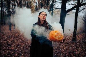 Young woman holding the halloween pumpkin with the white smoke coming from inside of it photo
