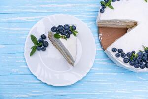 Appetizing cheesecake cake biscuit pillow decorated white cream blueberries and mint stands on wooden blue rustic table photo