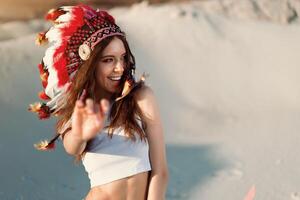 un hermosa joven caucásico niña en un blanco parte superior en su cabeza es vistiendo un indio sombrero. cucaracha es en el desierto. contento fiesta humor. foto