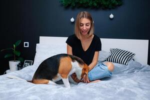 Young beautiful woman playing with dog sitting on bed in a stylish bedroom photo