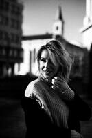 Smiling Woman in Jacket and Sweater Stands by Building. Confident Female Portrait in Urban Setting. Stylish Woman Poses Outdoors with Happy Expression. City Lifestyle Concept with Fashionable Woman photo