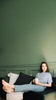 un pensativo joven de edad mediana mujer disfrutando un descanso y un taza de té en el sofá, reflexionando, mirando a el abierto espacio. pensativo momento. pensativo joven de edad mediana mujer descansa con té en sofá foto