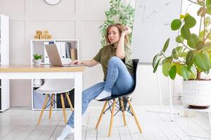 Business woman using laptop sitting desk white modern office interior with houseplant photo